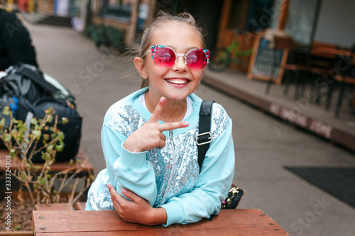 Little girl child wearing a sunglasses and backpack sitting n over city background