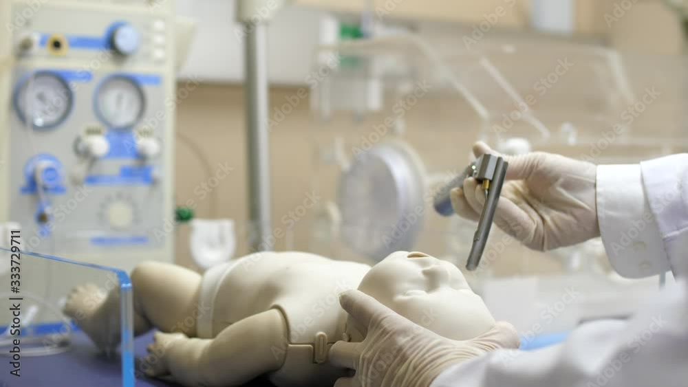 A pediatrician putting a laryngoscope on a newborn infant under a radiant warmer/resuscitator