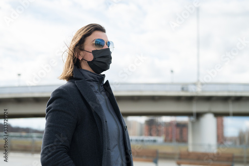 Fashionable stylish scared woman in protective black face mask, sunglasses, gray wool coat on the street near metro station. Self protection in transport during quarantine from coronavirus covid-2019