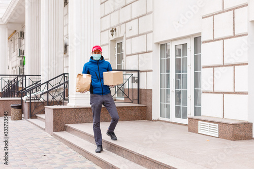 Courier in protective mask and medical gloves delivers takeaway food. Delivery service under quarantine, disease outbreak, coronavirus covid-19 pandemic conditions. © Angelov