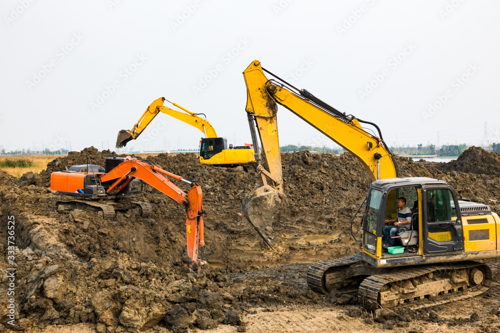 Digger working against a dramatic sky with another digger on the hill in the background Digger working against a dramatic sky with another digger on the hill in the background