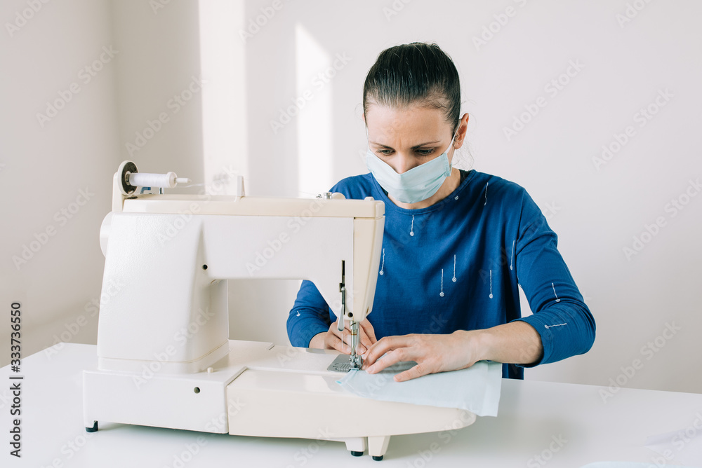 Woman hands using the sewing machine to sew the face home made diy medical mask during the coronavirus pandemia.