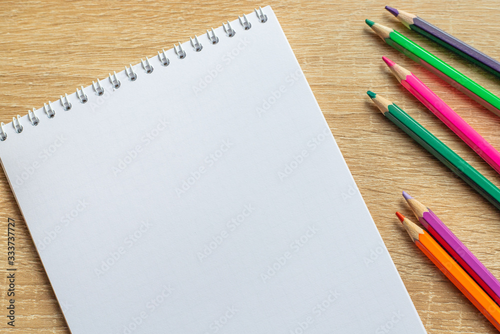 Notepad and colorful pencils on a wooden table. Top view Notepad and colorful pencils on a wooden table. Top view