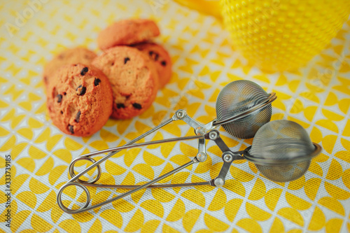 Tea time, yellow tea cup and cookies on the table. Mesh tea stainer on yellow table with leaf tea around. photo