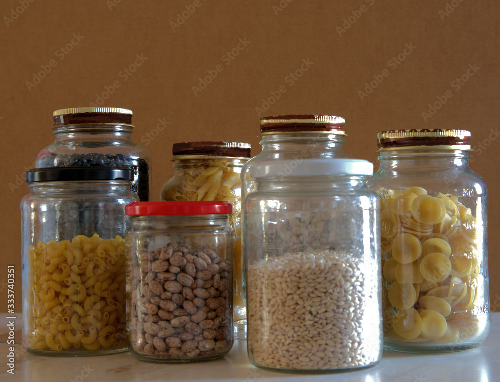Glass jars with dried food stuffs on a pantry shelf. Glass jars with dried food stuffs on a pantry shelf.