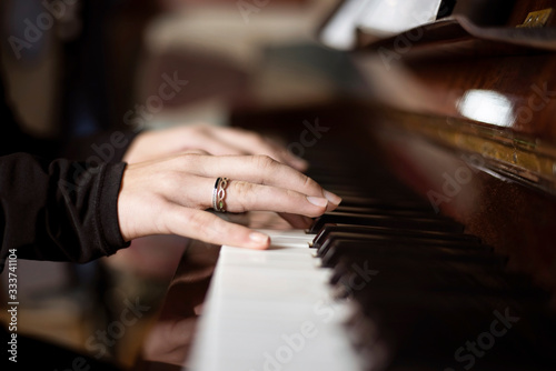 The hands of a young girl on the keys of the piano play a familiar melody, close up. The girl loves playing the piano since childhood