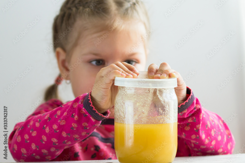 Caucasian child of three years old trying to pull off cover from jar with honey indoor Caucasian child of three years old trying to pull off cover from jar with honey indoor