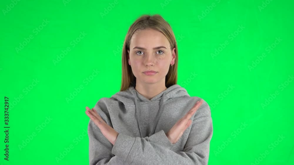 Portrait of young woman with blond hair strictly gesturing with hands crossed making X shape meaning denial saying NO on greenscreen Portrait of young woman with blond hair strictly gesturing with hands crossed making X shape meaning denial saying NO on greenscreen