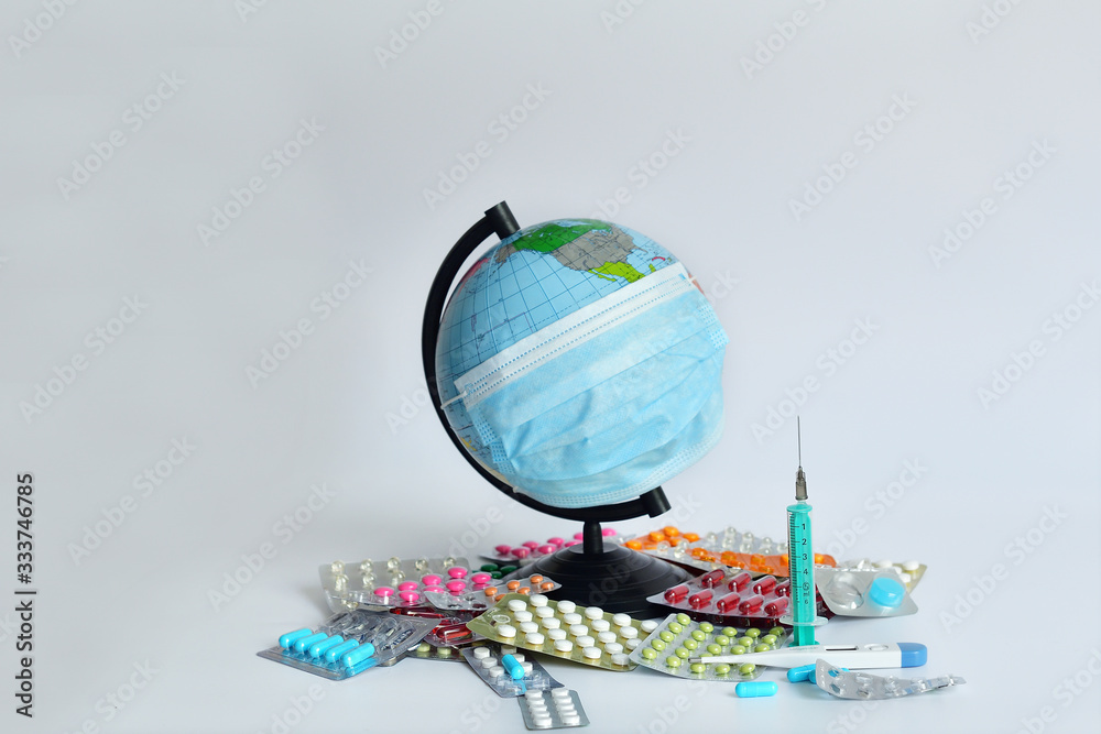 Obraz premium Globe in a medical mask against the background of pills.the globe is wearing a medical mask on white background. the inscription of a world pandemic. covid-19