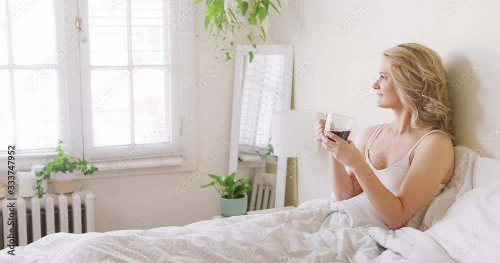 Medium Shot of an attractive young blond woman enjoying her cup of coffee at home as she looks out the window. Medium Shot of an attractive young blond woman enjoying her cup of coffee at home as she looks out the window.
