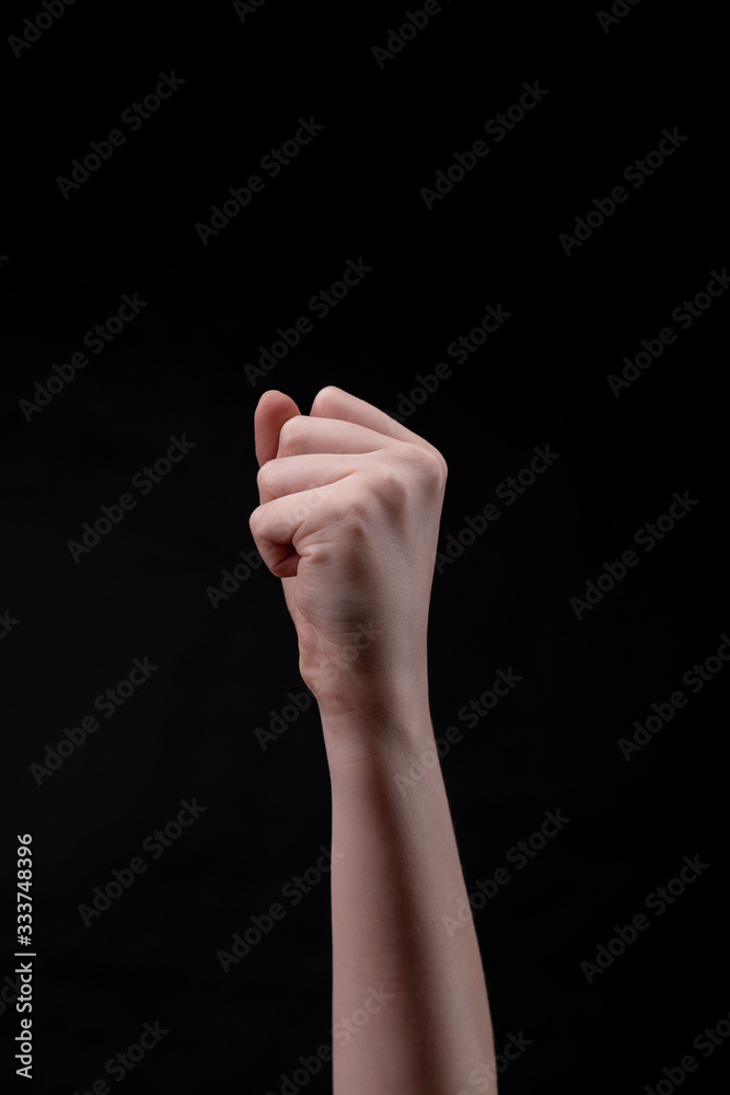 A fist on a black background. Beautiful girl's hand raised up. Minimalism. Protest sign A fist on a black background. Beautiful girl's hand raised up. Minimalism. Protest sign