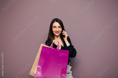 Beautiful well-dressed young girl holding a blank paper bag and shopping at an online store against a wall background with copy space for text or design. Horizontal layout