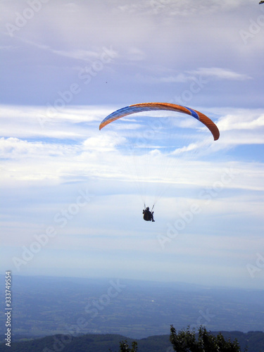 Épine mountain, France - August 5th 2008 : Focus on a blue and orange paraglider in mid flight. We can see the green countryside of the French Alps in the background.
