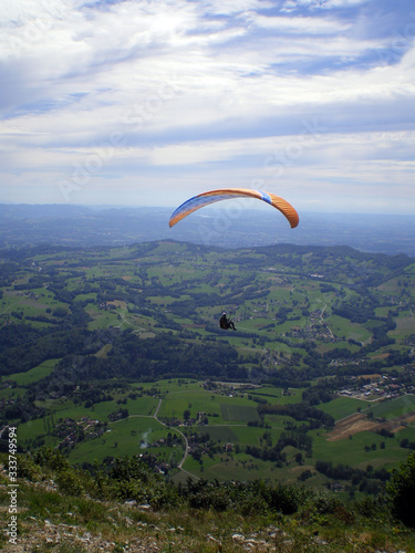 Épine mountain, France - August 5th 2008 : Focus on a blue and orange paraglider in mid flight. We can see the green countryside of the French Alps in the background.