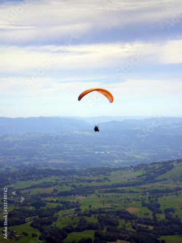 Épine mountain, France - August 5th 2008 : Focus on a purple and orange paraglider in mid flight. We can see the green countryside of the French Alps in the background.