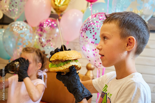 The handsome little boy eating burger in black rubber gloves.