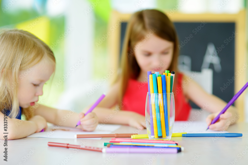 Two sisters drawing with colorful pencils at home. Creative kids doing crafts together. Education and distance learning for kids. Homeschooling during quarantine. Stay at home entertainment. Two sisters drawing with colorful pencils at home. Creative kids doing crafts together. Education and distance learning for kids. Homeschooling during quarantine. Stay at home entertainment.