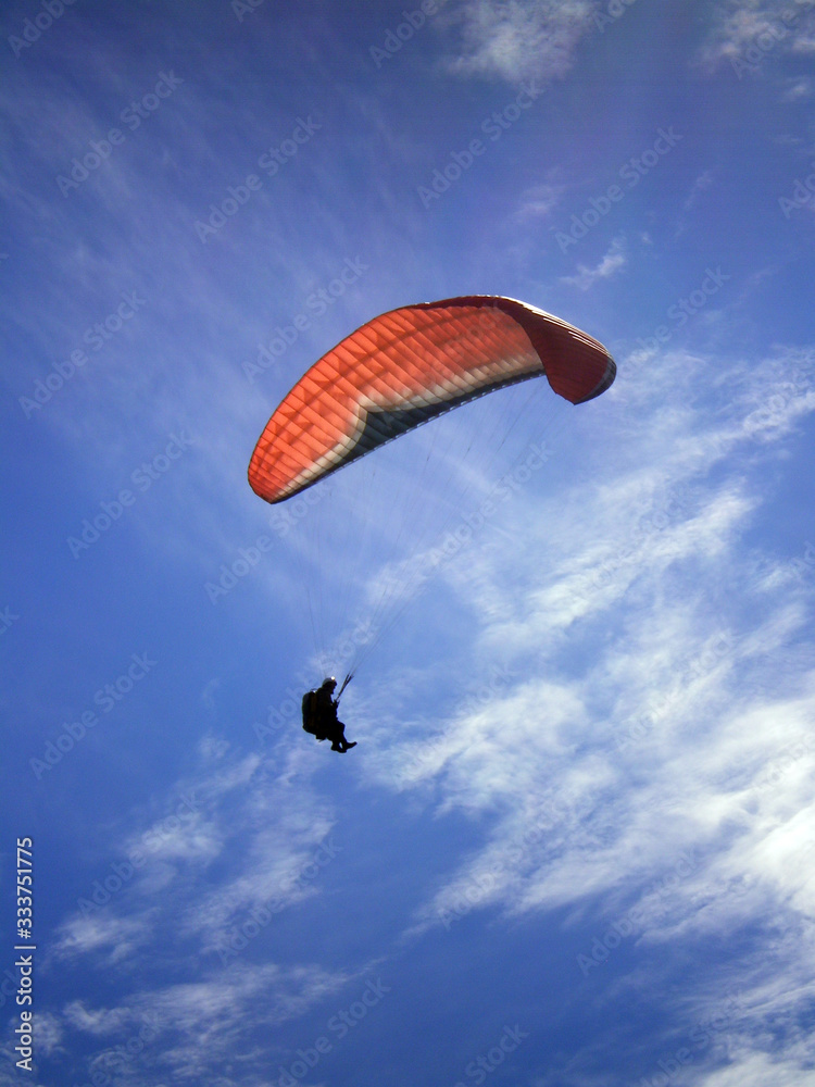 Épine mountain, France - August 5th 2008 : Focus on a blue and orange paraglider in mid flight. We can see a beautiful blue sky in the background. Épine mountain, France - August 5th 2008 : Focus on a blue and orange paraglider in mid flight. We can see a beautiful blue sky in the background.