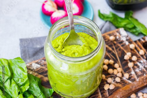 Green spinach chickpea hummus in glass jar. Vegan, vegetarian healthy food.