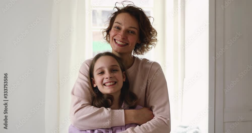 Happy affectionate young mom hugging teen daughter looking at camera standing at home. Smiling adult parent single mother embracing cute teenage adolescent girl posing together indoor. Family portrait Happy affectionate young mom hugging teen daughter looking at camera standing at home. Smiling adult parent single mother embracing cute teenage adolescent girl posing together indoor. Family portrait