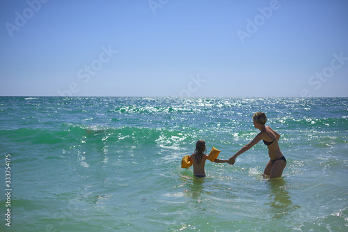 Summer happy family of six years blonde child playing and jumping water waves embracing woman mother in sea shore beach © sarymsakov.com