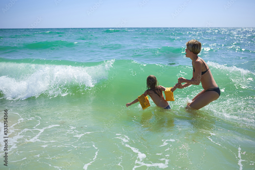 Summer happy family of six years blonde child playing and jumping water waves embracing woman mother in sea shore beach Summer happy family of six years blonde child playing and jumping water waves embracing woman mother in sea shore beach