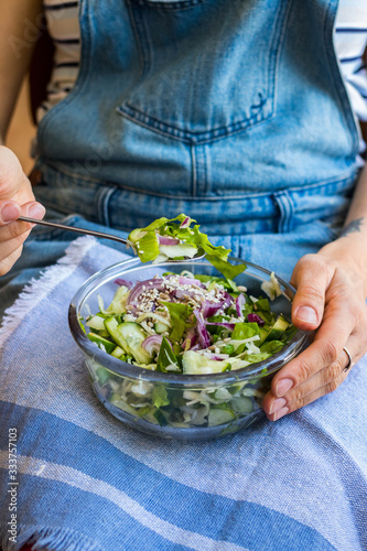 Detox vitamin green fresh salad in bowl. Mix of vegetables and herbs. Cucumbers, red onion, salad leaves. Woman holds in hands on legs bowl of vegan salad. Healthy food.