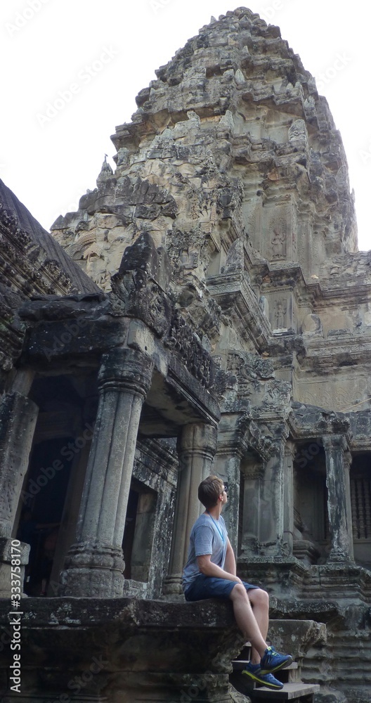 Young man sitting and looking up at stone pyramid of Angkor, ruins of Angkor, Cambodia Young man sitting and looking up at stone pyramid of Angkor, ruins of Angkor, Cambodia