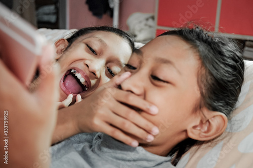 Southeast Asian ethnicity teenage girls siblings laughing together haviing fun viewing information from social media through smartphone