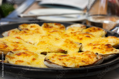 Baked clams covered with parmesan cheese. Closeup on traditional Chilean meal on hot black plate. Gourmet restaurant food concept