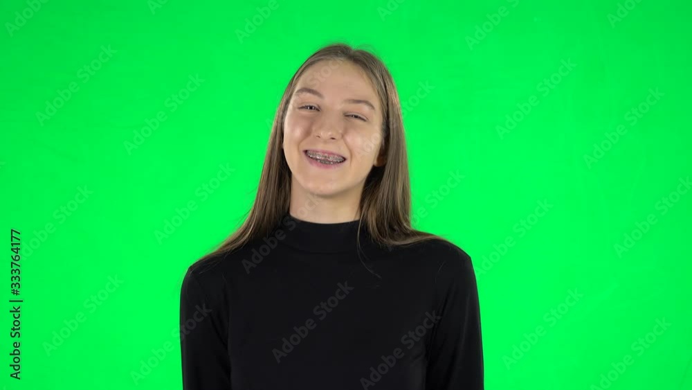 Portrait of awkward teenage girl is wearing braces smiling while cheerful looking at camera on a green screen Portrait of awkward teenage girl is wearing braces smiling while cheerful looking at camera on a green screen
