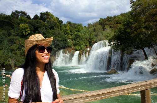 happy smiling female asian tourist standing by waterfalls Krka in national park in Croatia in summertime 