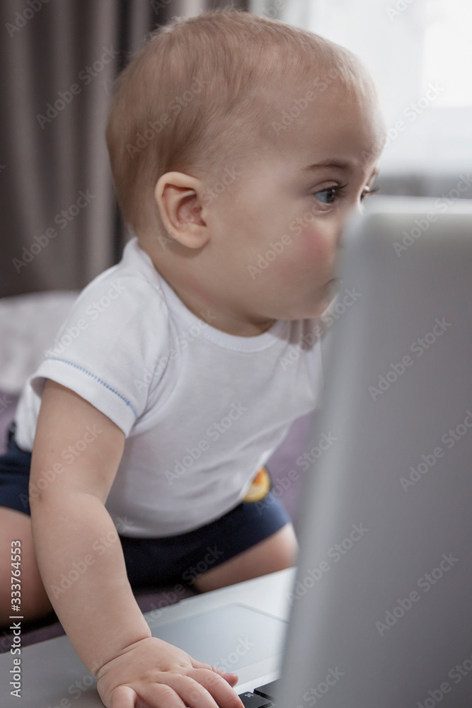 The baby looks with interest at the laptop screen. New generation. Close-up. Vertical.
