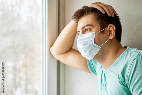 A man with a protective medical mask at the window. Quarantined, isolated from society.
