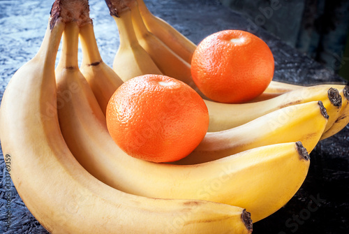 Bananas and orange with reflection in the mirror on a black background.