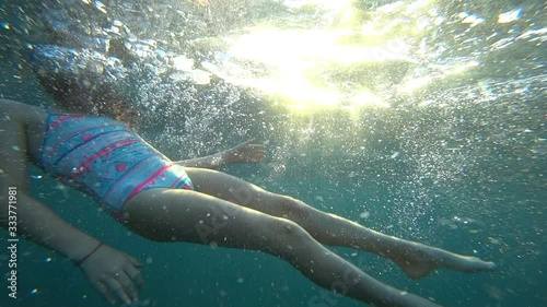 Young girl having fun in clear blue ocean underwater with snorkel or diving mask.