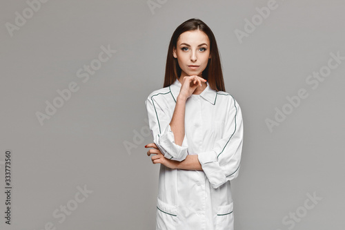 Young woman in white medical coat posing at the grey background, copy space for your advertising. Healthcare concept. Female model in the image of a doctor photo