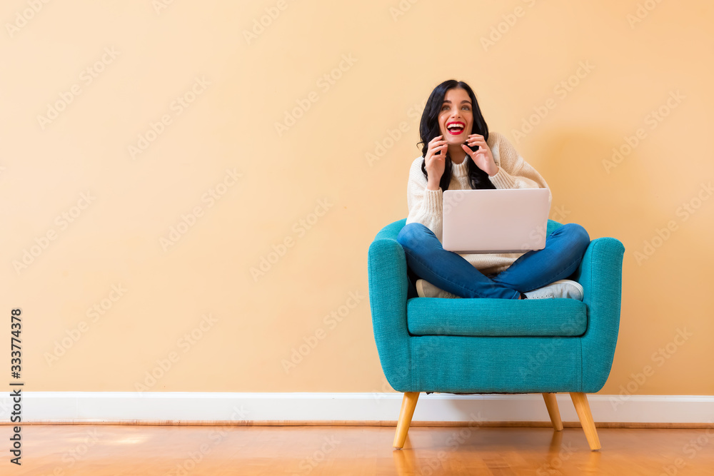 Surprised young woman using a laptop computer sitting in a chair