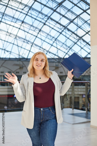 blonde girl in a jacket stands with a folder in a business center body positive