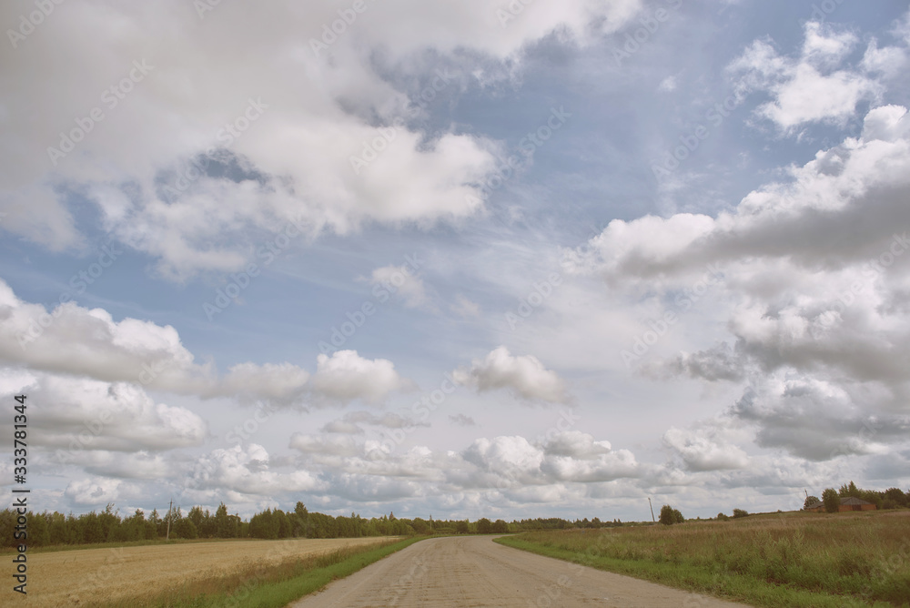 road in a field under a blue sky with clouds