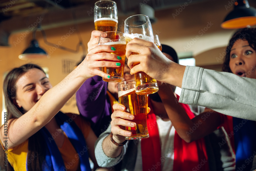 Sport fans cheering at bar, pub and drinking beer while championship, competition is going. Multiethnic group of friends excited watching translation. Human emotions, expression, supporting concept.