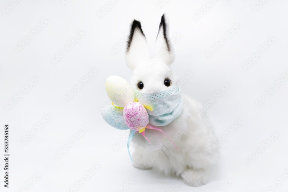Obraz premium Easter Bunny in a facial medical mask with a bouquet of colorful eggs. The concept of Easter and quarantine during coronavirus. Like a postcard wishing you well