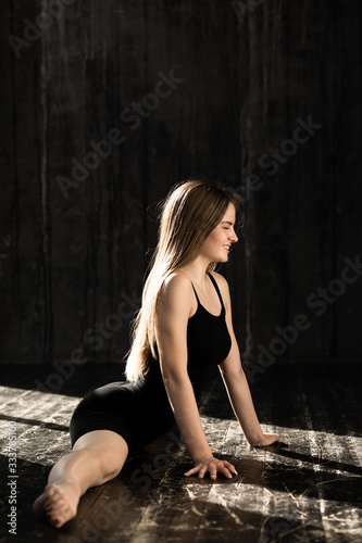 Beautiful athletic woman in black clothes sits on a split. Gymnast does stretching before exercise. © DmitryStock
