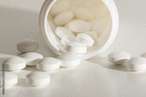 Spilled white medicine pile of prescription pills in a white bottle on a white background