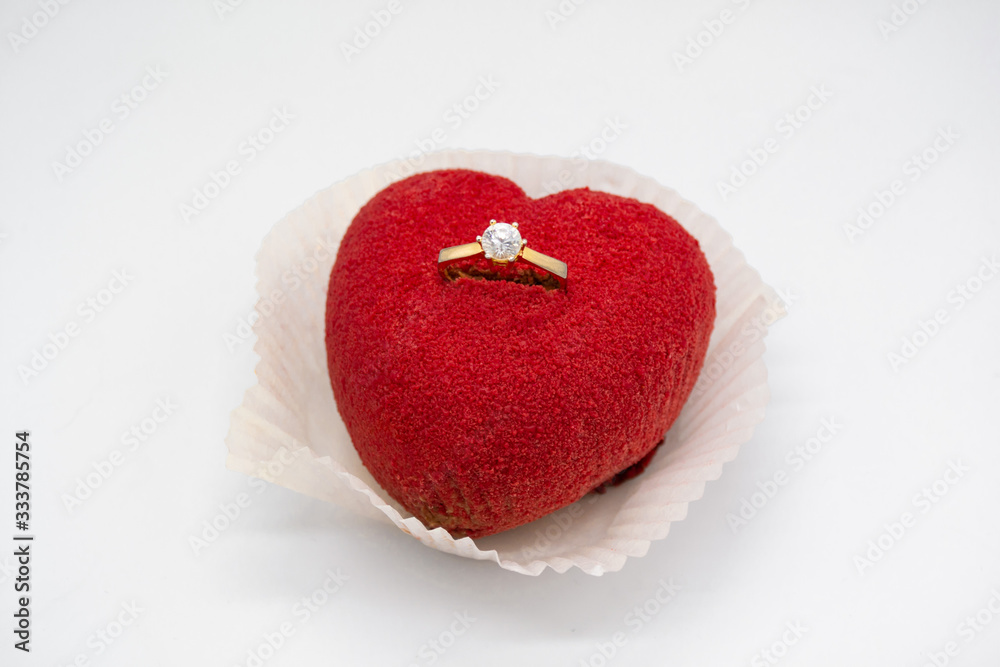 A bright red heart-shaped cake with a gold diamond engagement ring inside A bright red heart-shaped cake with a gold diamond engagement ring inside