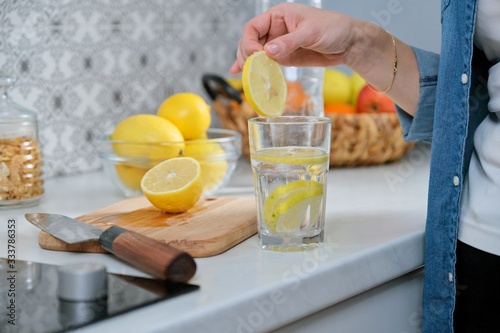 Female hand with slice of lemon in kitchen, with sparkling water with lemon