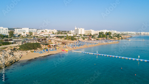 Aerial bird's eye view of Fig tree bay in Protaras, Paralimni, Famagusta, Cyprus. Famous tourist attraction golden sand family beach with boats, sunbeds, water sports pier, swimming in sea from above.