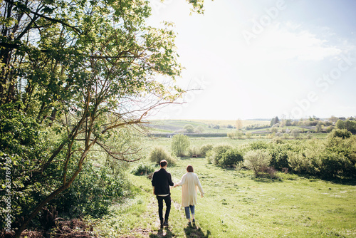 Lifestyle couple walking on grass in field on sunny day. Hug, kiss, hold hands, have fun. Warm photo with lens flare