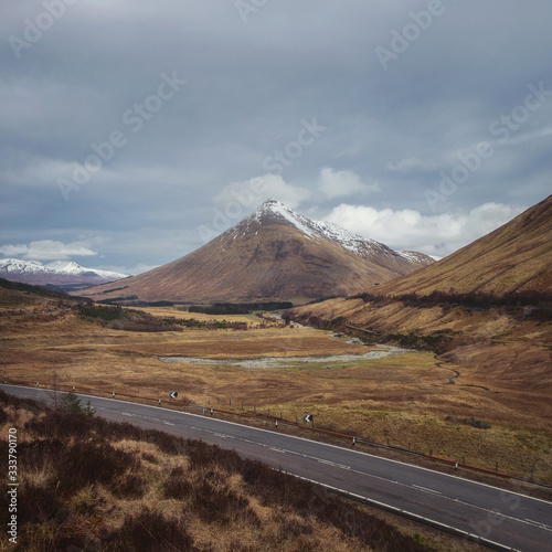 Open road leading through the Scottish Highlands of Glen Coe, snowcapped mountains, and river valley