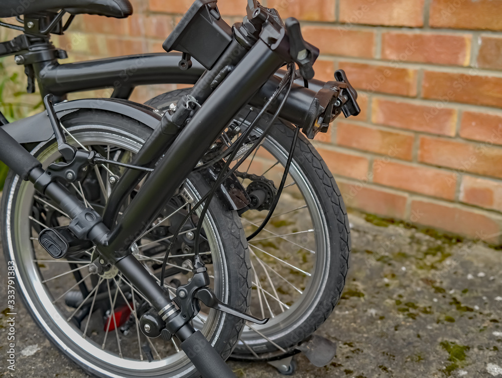  Close up of a black folding bicycle in front of a red brick wall